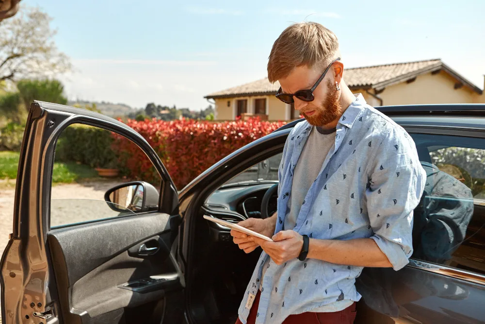 Bărbat care verifică pe tabletă detalii despre o mașină second-hand, lângă ușa deschisă a automobilului